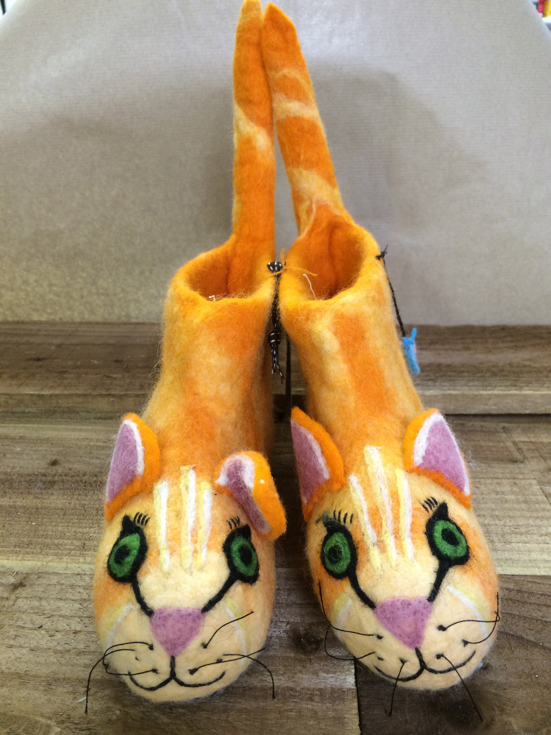 Ginger cat shaped felted slippers on a wooden background.