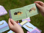 Two hands holding educational cards about tree wasps and common wasps with illustrations on a grassy background.