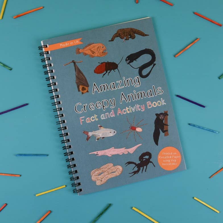 Book titled 'Amazing Creepy Animals Fact and Activity Book' on a blue background with colorful pencils.