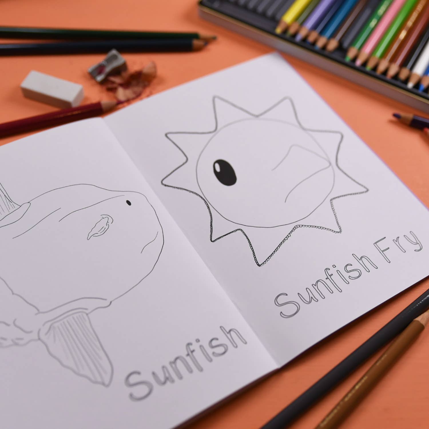 Coloring book with sunfish drawing and coloring supplies on an orange surface