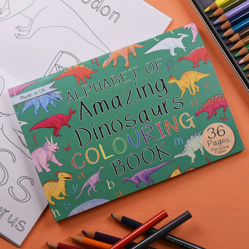 Colouring book titled 'Alphabet of Amazing Dinosaurs' with crayons and coloring sheets on an orange surface.