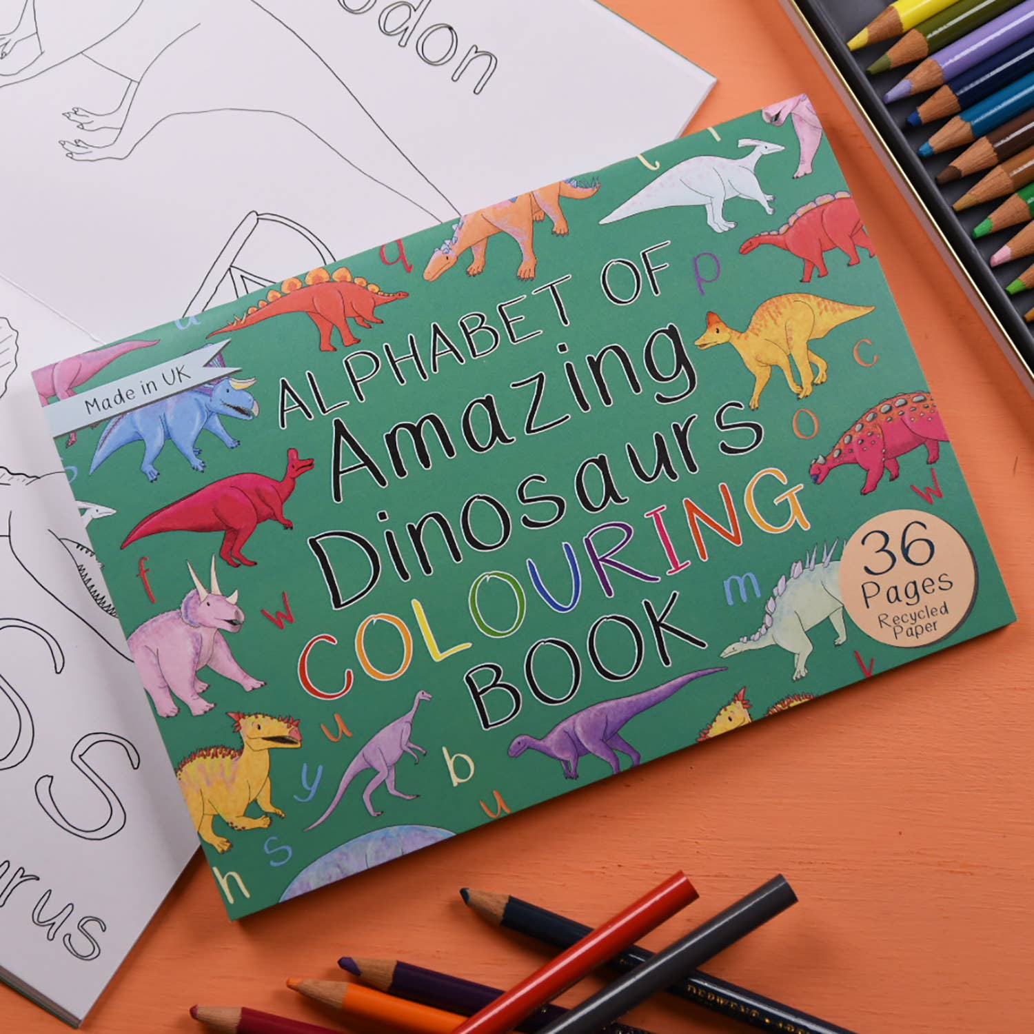Colouring book titled 'Alphabet of Amazing Dinosaurs' with crayons and coloring sheets on an orange surface.