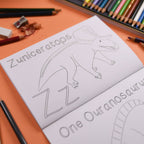 Colouring book with dinosaur illustrations and coloring pencils on an orange surface