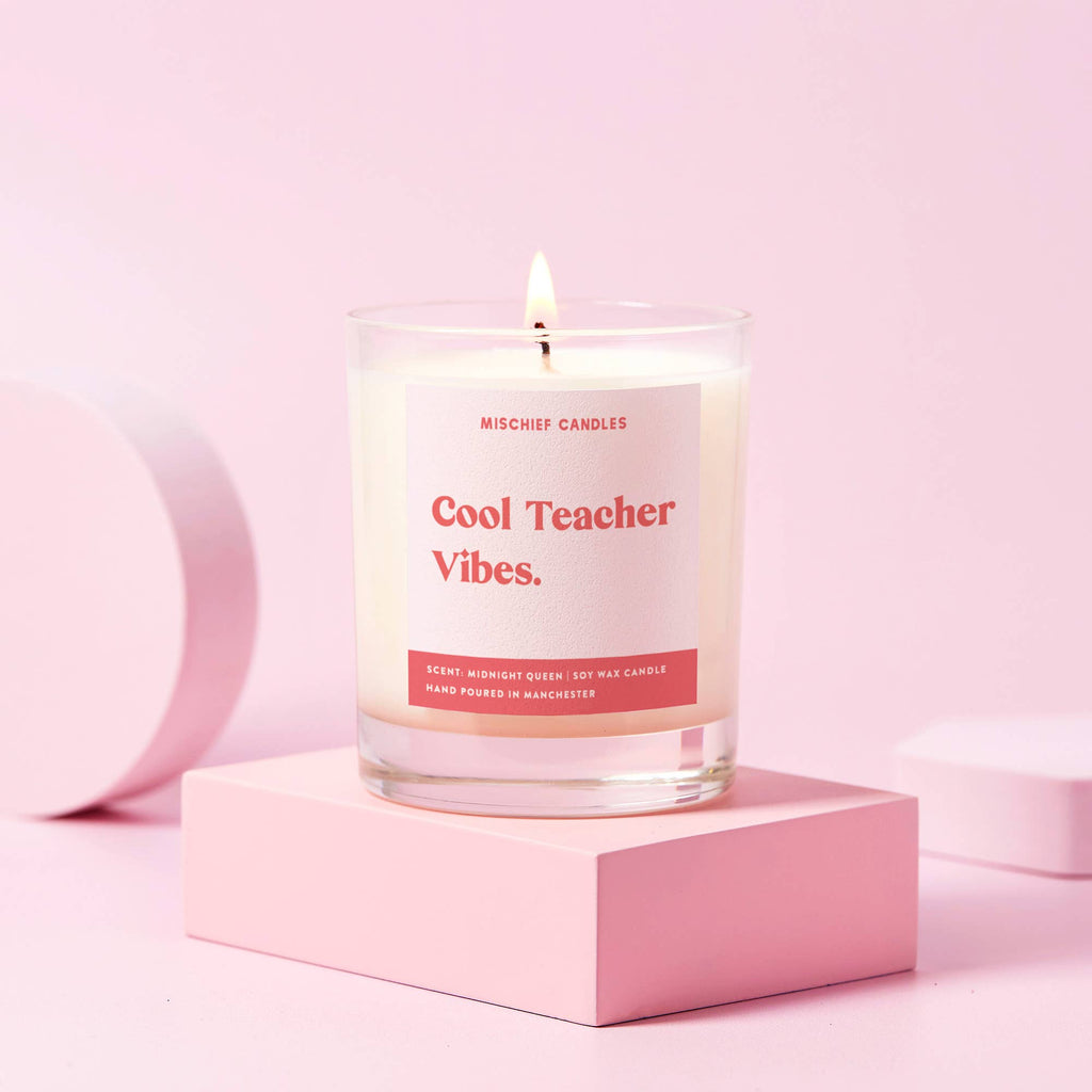 A candle with a pink label reading 'Cool Teacher Vibes' on a pink pedestal, with a pink background.