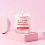 Candle with a pink label on a pink surface, label reads 'let go of things that make you fucking miserable"