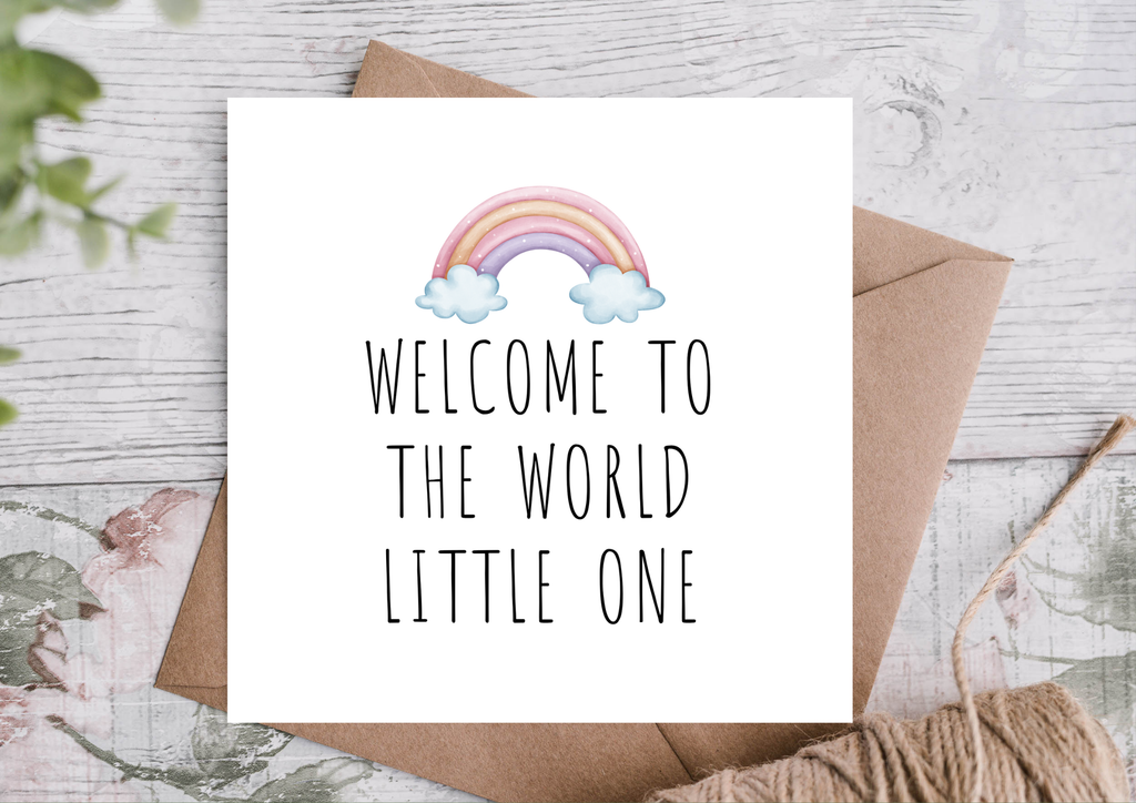 Greeting card with rainbow and 'Welcome to the World Little One' text on a wooden surface.