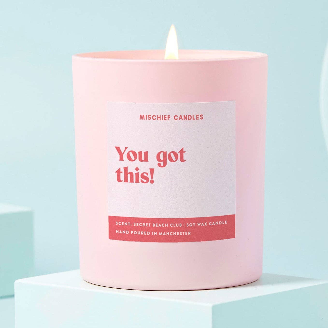 A pale pink candle with bold red text that reads 'You Got This' on a white background, with the brand.