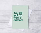 Green card with text 'You still look 25 from a distance' on a light gray wooden surface