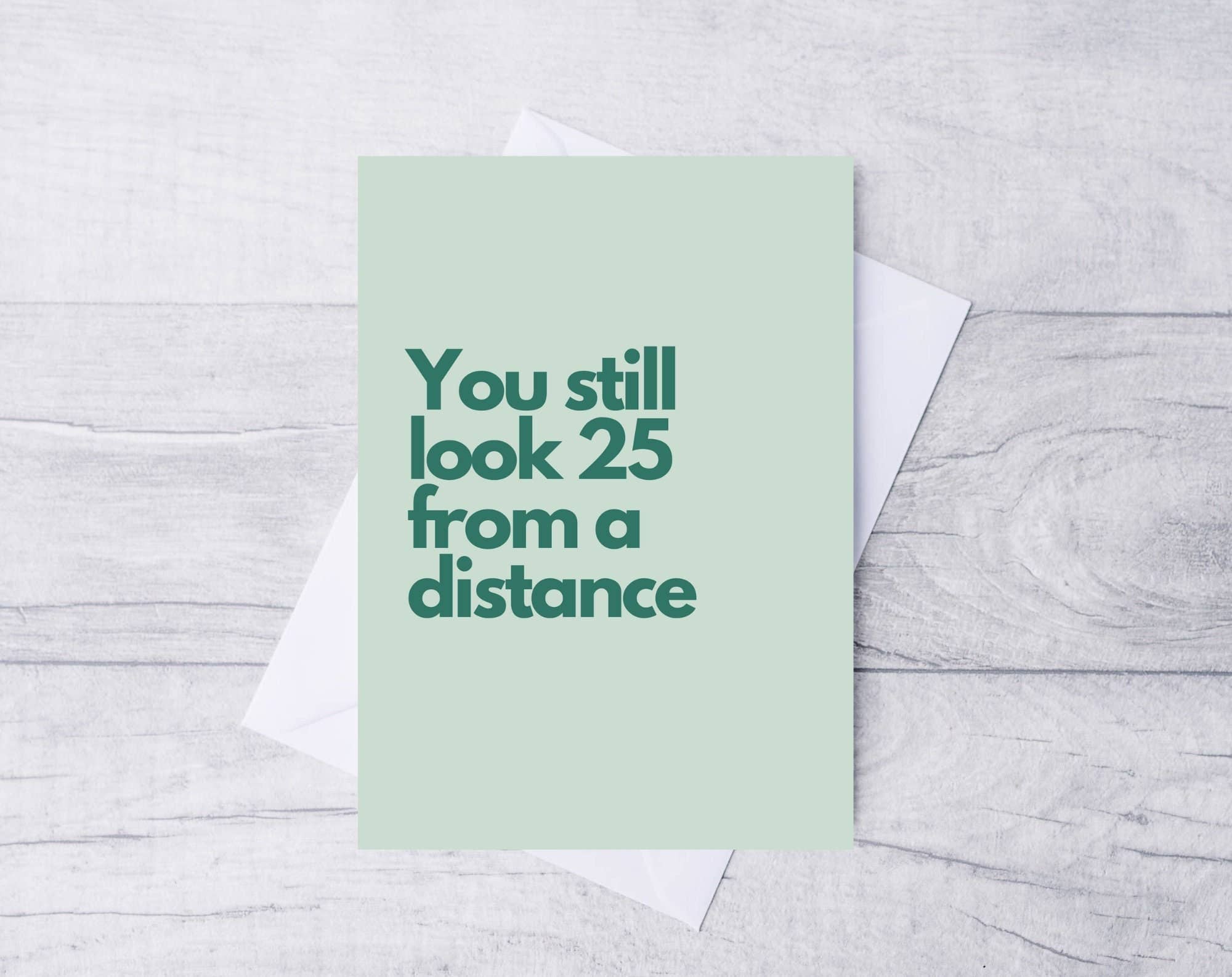 Green card with text 'You still look 25 from a distance' on a light gray wooden surface